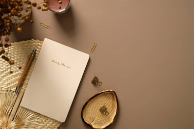 Estetik ofis masası. Haftalık ajandası, kalemi, ofis kâğıdı, mumu, kurutulmuş çiçekleri olan kadınsı çalışma alanı. Düz yatış, üst görünüm.