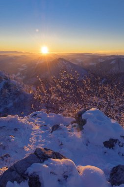 At the top of the snowcapped mountain lit by setting sun in background in winter. Achievement, hiking, mountaineering, travel and environment concepts.