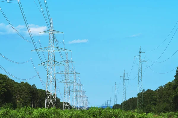 Long line of transmission towers on deforestated strip going through forest area. Electricity, power transmission and distribution, electrical energy, clean energy and environment concepts