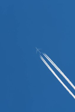 Passenger airplane on a blue sky with visible trail of condensed water vapor and combusted jet fuel. Travel, air traffic and environment concepts