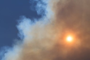 Güneş, arka planda mavi gökyüzü olan bir duman bulutu tarafından gizleniyor. Yangınlar, çevre ve kirlilik kavramları