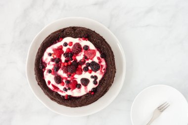 Çikolatalı, unsuz, taze kremalı ve mermer zemin üzerinde donmuş yaz meyveleri. Üst görünüm.