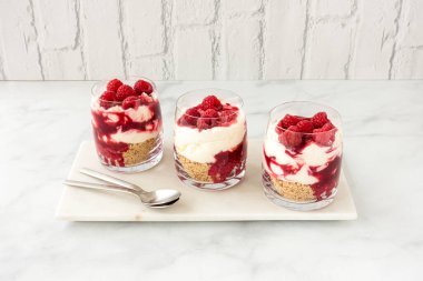 Üç bardak beyaz mermer üzerine ev yapımı ahududu tatlısı ve arka planda beyaz tuğla duvar. Açılı görünüm ve kopyalama alanı.