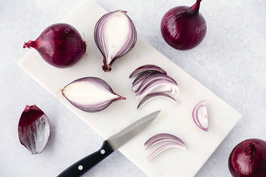 Red raw onions, whole, halved, quartered and sliced on white marble chopping board with knife. High angle view and copy space.