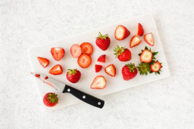 Tam, kesilmiş, dilimlenmiş, dörde bölünmüş ve yarım çilek beyaz mermer kesim tahtası üzerinde mermer arka planda fotokopi alanı ile. Üst Manzara. Yatay Sürüm.