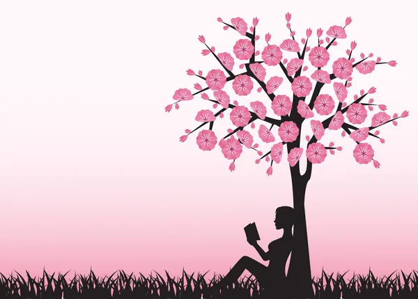 Kadın ağacın altında kitap okuyor.