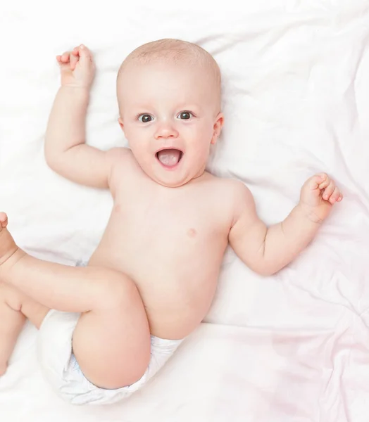 Laughing baby in diaper laying on the white bed — Stock Photo, Image