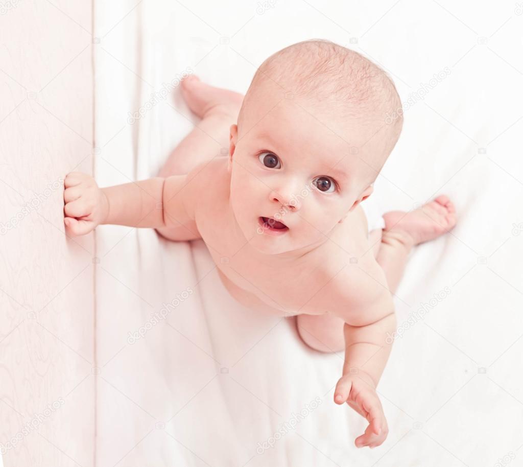 Baby in diaper sitting on the white bed