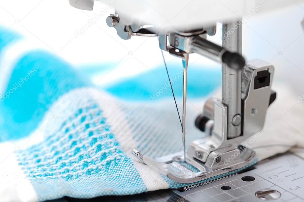 Sewing machine closeup with blue fabric on white background