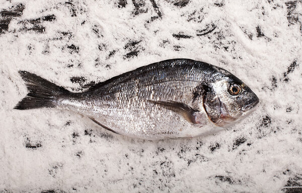 Свежая рыба Дорадо на фоне соли и темного дерева
