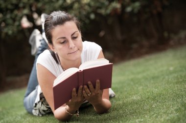 genç güzel kadın yeşil alan üzerinde uzanır ve kitap okuma.