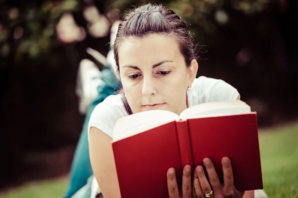 Jonge mooie vrouw legt op groene veld en leest boek. — Stockfoto