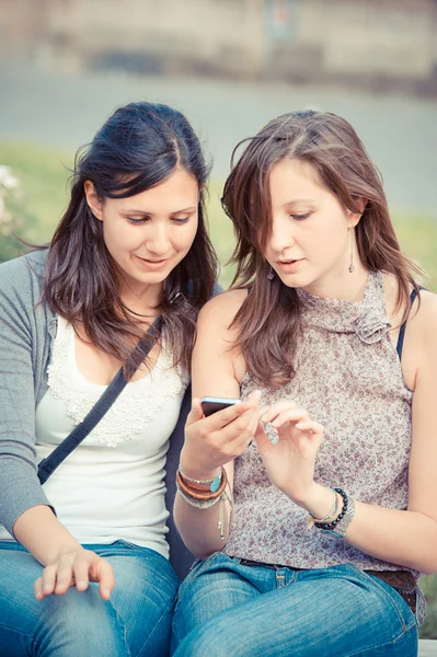 Two shopping girls in park with a mobile phone Stock Picture