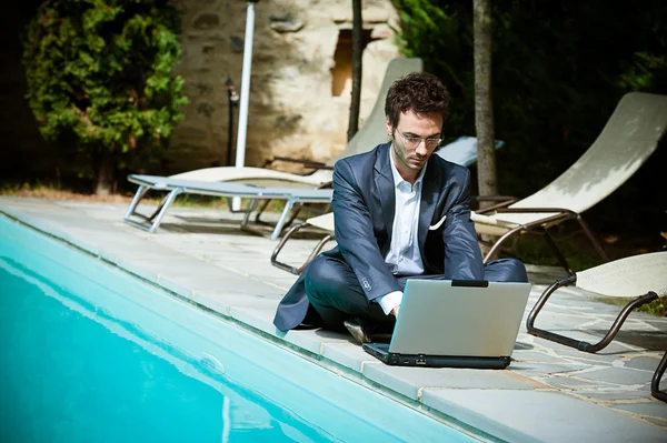 Jungunternehmer mit Computer neben Schwimmbad — Stockfoto