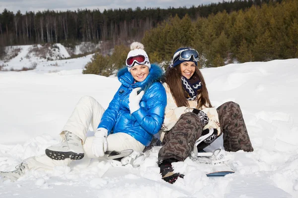Две девушки с сноубордами сидят на снегу — стоковое фото