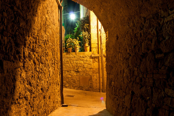 Mysterious narrow alley with lanterns at night, Pienza Italy