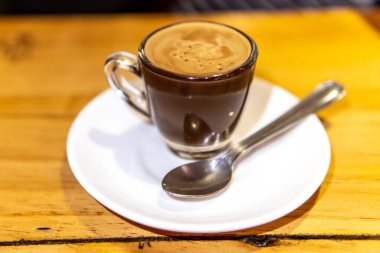 Beyaz tabakta kaşık olan bir bardak kahve.