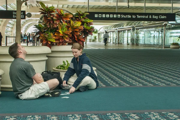 Man & Woman Pass Time with Card Games at Airport — Stock Photo, Image