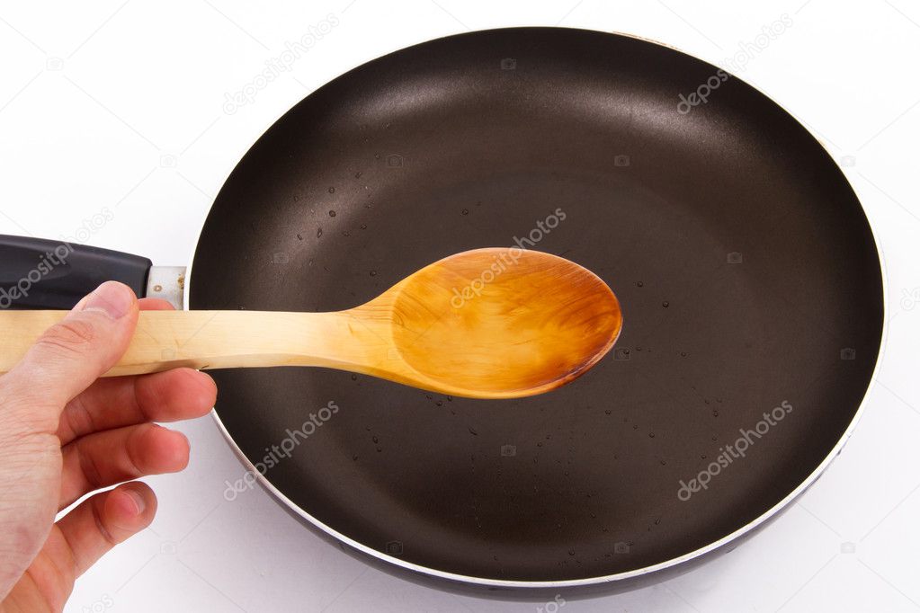 Hand Holding Spoon over Frying Pan