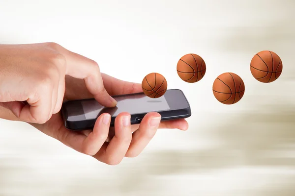 Рука с помощью смартфона с баскетбольным предметом — стоковое фото