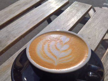 Daire üzerinde kapuçino kahveli siyah bir porselen fincan parlak güneş ışınlarının altında gri ahşap tahtalar üzerinde duruyor.