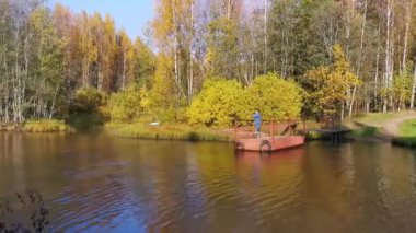 Bir adam küçük bir demir feribotla sessiz bir nehri geçer.