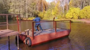 Bir adam küçük bir demir feribotla sessiz bir nehri geçer.