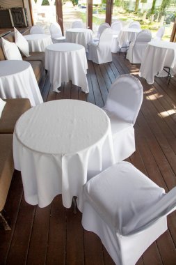 Beyaz masa örtülerinin altında açık bir kafe restoranında kar beyazı masalar ve sandalyeler.