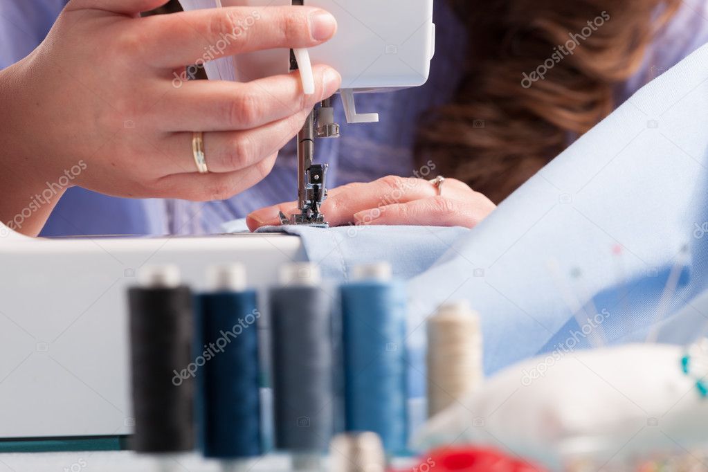 Hands on sewing machine with reels of colour threads and sewing