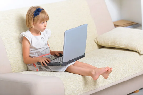 Liten flicka sitter i soffan med laptop — Stockfoto