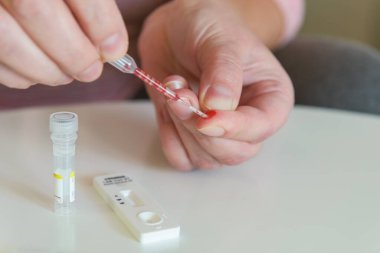 Kadın, COVID19 testi yapmak için parmağından bir pipetle kan örneği alıyor.