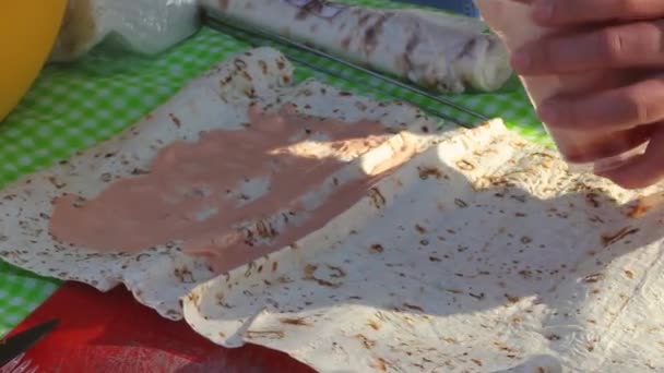 女性の手は冬のピクニックで野菜の肉のロールのためのフォークでピタにトマトソースを入れ 冷たい外で自家製ツイストファーストフード — ストック動画