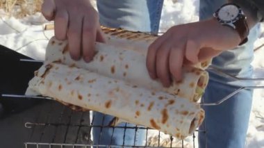 Erkek eli, piknikte piknikte mangal kafesinde sebze ve et rulosu çevirir. Soğuk kampta ev yapımı sıcak ızgara fast food.