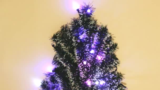 Las luces de Navidad parpadean en el árbol de Navidad en el fondo amarillo para los telones de fondo festivos, vista superior de las vacaciones brillando — Vídeo de stock