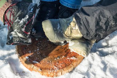 Tahta ayaklar üzerinde yürüyüş yapan insan bacakları, güneşli kış gününde kamp alanında dinlenen bir grup arkadaş, vahşi doğada dinlenmek.