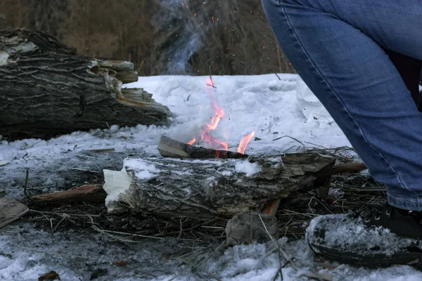 Gamba maschile dal falò invernale al campeggio crepuscolo in natura, tronco d'albero due e piccolo fuoco sulla neve, umore campeggio Immagine Stock