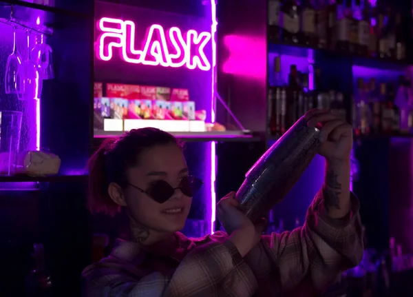 Barista donna con shaker cocktail in nightclub bar con luce viola viola e rosa rossa al neon, barman al club party Foto Stock