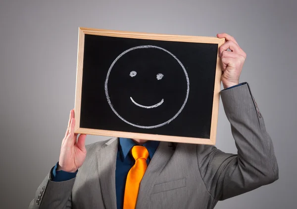 Businessman hiding his face with a white billboard with a smiley — Stock Photo, Image