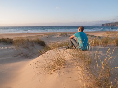 Bir kumul üzerinde oturan ve bir plaj sahne zevk adam
