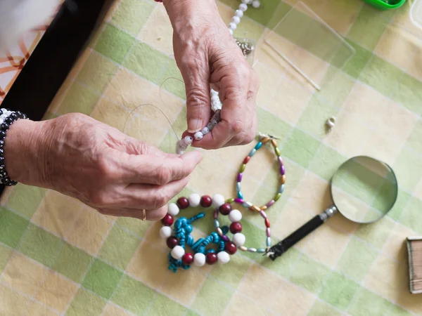 Mãos de mulher sênior fazendo um colar — Fotografia de Stock