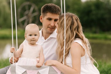 Güzel küçük bir kız, anne ve babasıyla birlikte bir sepetin içinde balonla ve bir pastayla ilk doğum gününü kutluyor.