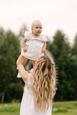Doğada bir yaşında bir kızı olan güzel, genç bir anne. Anne gülümseyip kızını fırlatıyor.