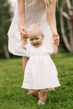 Doğada bir yaşında bir kızı olan güzel genç bir anne, bir kız ilk adımlarını atar.