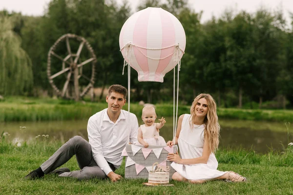 一个漂亮的小女孩带着妈妈和爸爸 带着气球和蛋糕 在篮子里庆祝她的第一个生日 — 图库照片