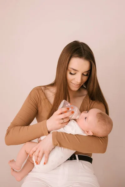 一位慈眉善目的年轻母亲用浅色背景的瓶子喂她刚出生的女儿 — 图库照片