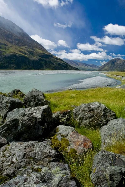 Gray rocks on the banks of a mountain stream with a view to the mountains of the Naumann Range, South Island, New Zealand, Oceania
