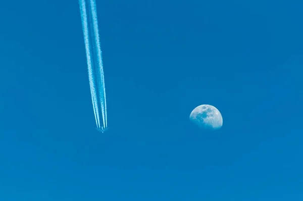 Airplane with condensation trail and moon on blue sky