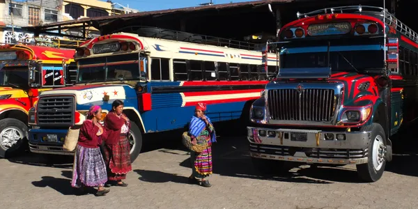 Tres mujeres nativas con ropa tradicional caminan cerca de autobuses de colores en el mercado —  Fotos de Stock