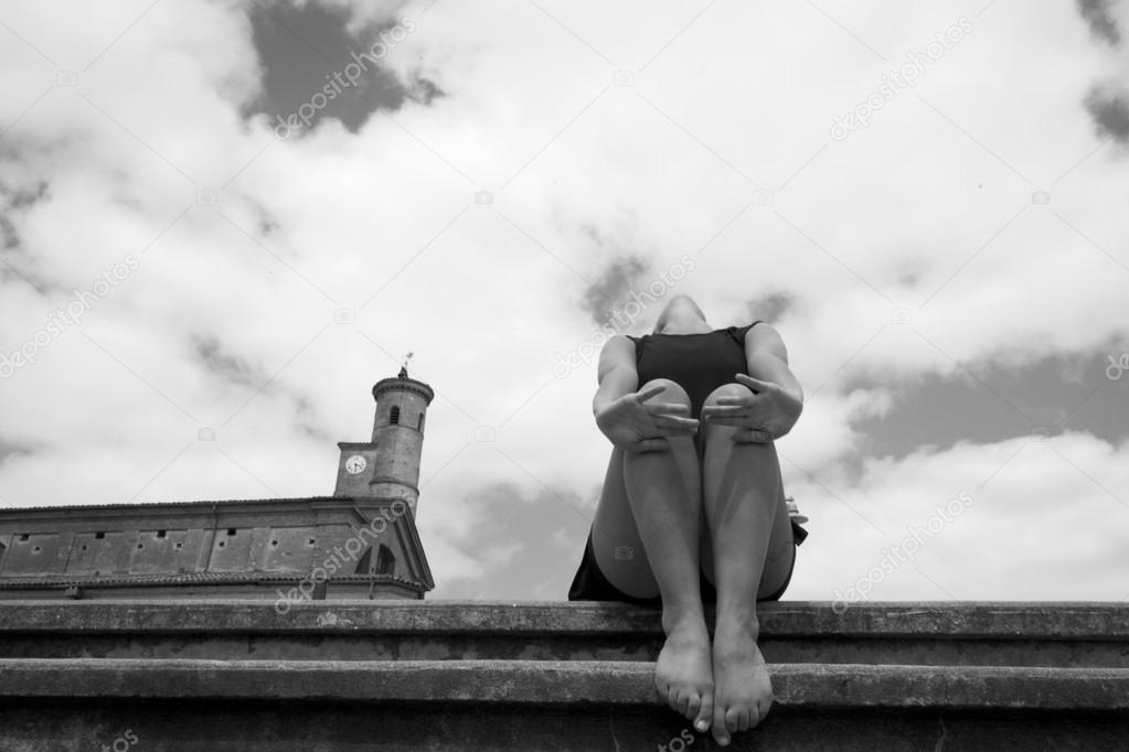 Barefoot dancer is sitting on stone stairs, outdoors