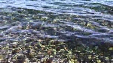 Deniz çakıl taşı plajı, çok renkli taşlar, köpüksüz şeffaf dalgalar, güneşli bir sonbahar gününde.